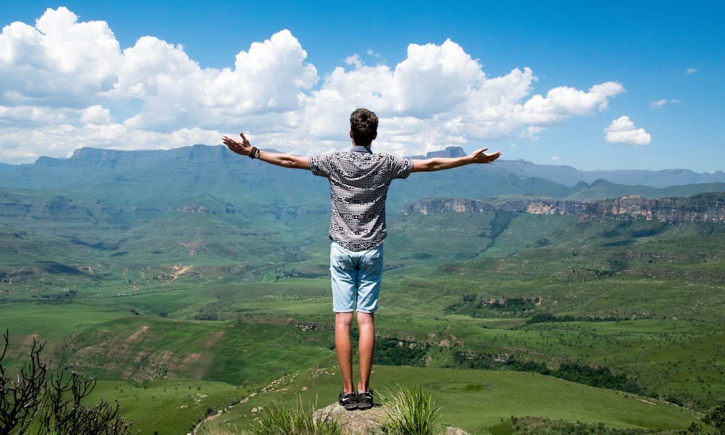 A man stands triumphantly with arms open, overlooking a scenic mountain range.