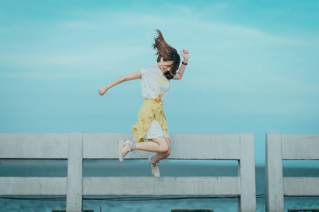 Woman jumping cheerfully on a bridge under a sunny blue sky, embodying freedom and happiness.