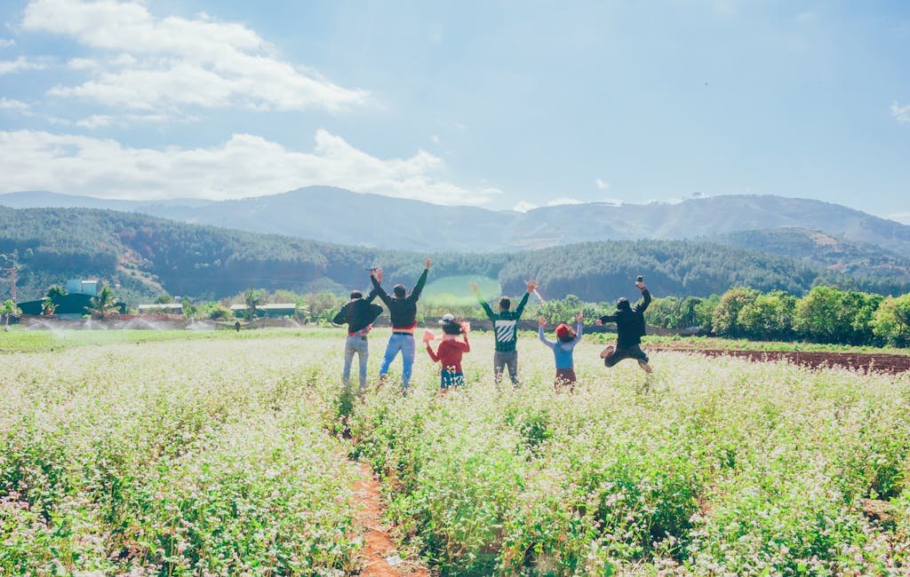 A group of people jumping with joy in a beautiful countryside field surrounded by mountains and clear skies.