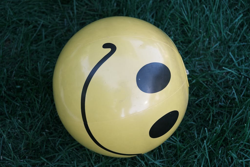 Close-up of a yellow smiley face ball resting on green grass.