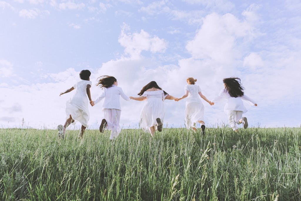 Five women running hand in hand in a grassy field, symbolizing freedom and happiness.