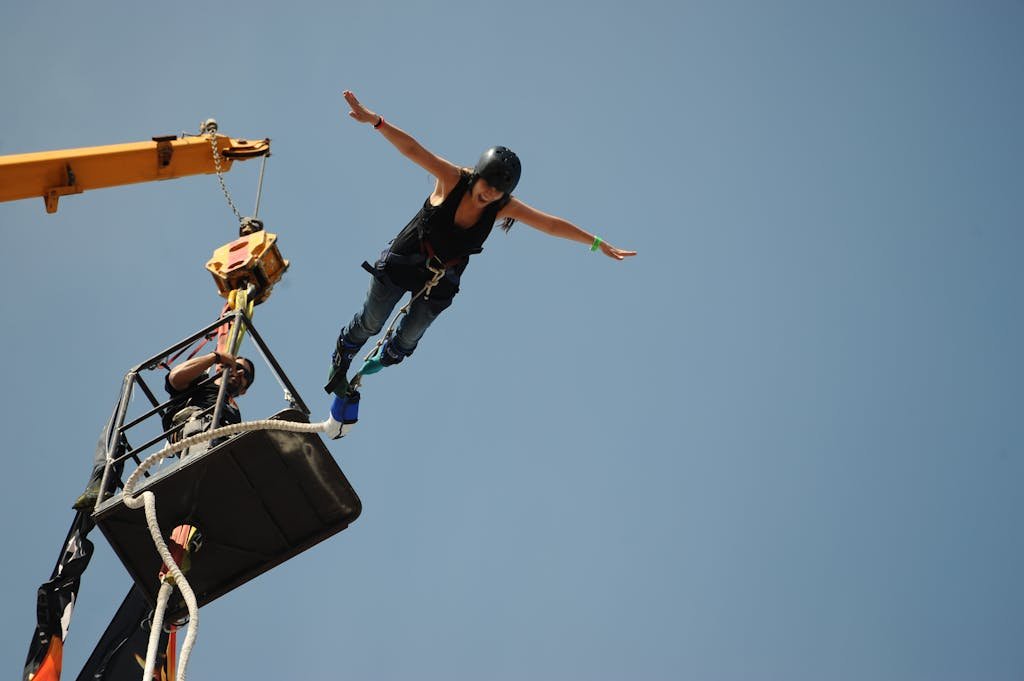 Thrill-seeker leaps from platform during bungee jumping with arms spread wide, experiencing freedom and adrenaline.