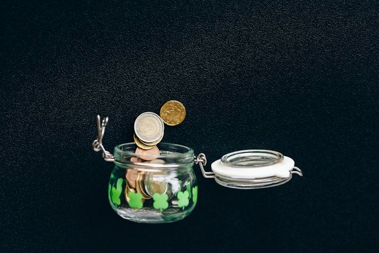 Glass jar with coins falling into it on a black background, symbolizing savings.